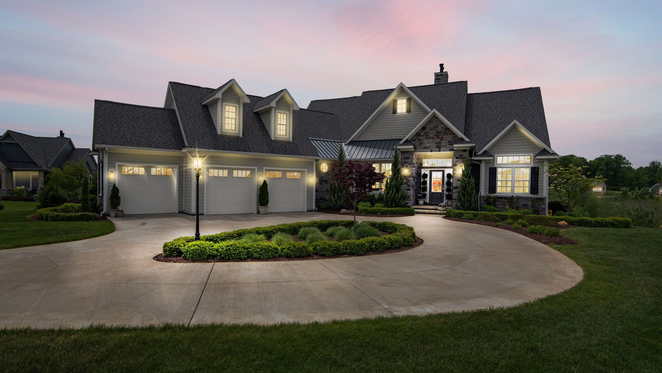 Custom-built home at dusk with warm interior lighting, landscaped grounds, and a paved drive