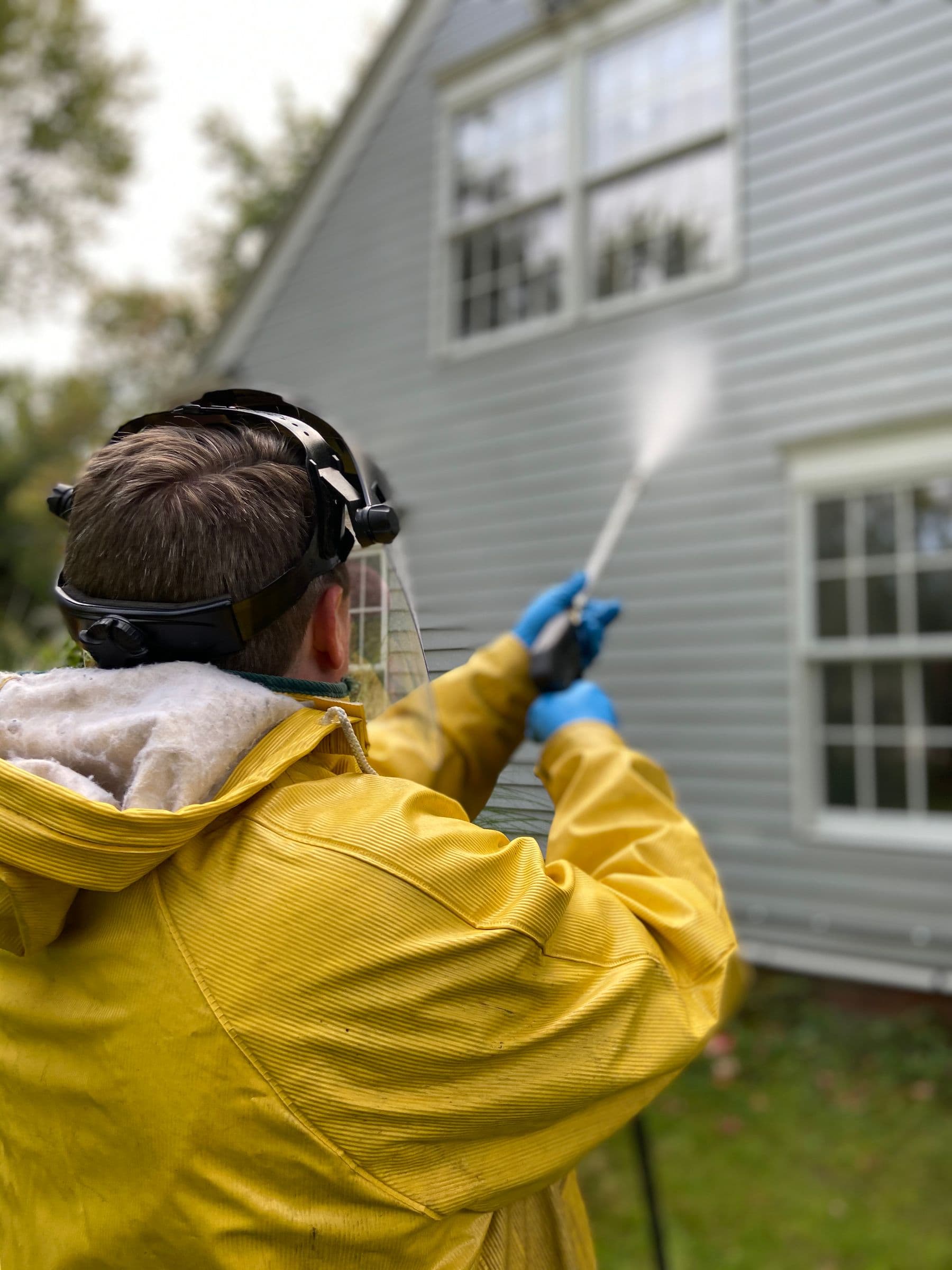 Technician in protective gear pressure washing the side of a house